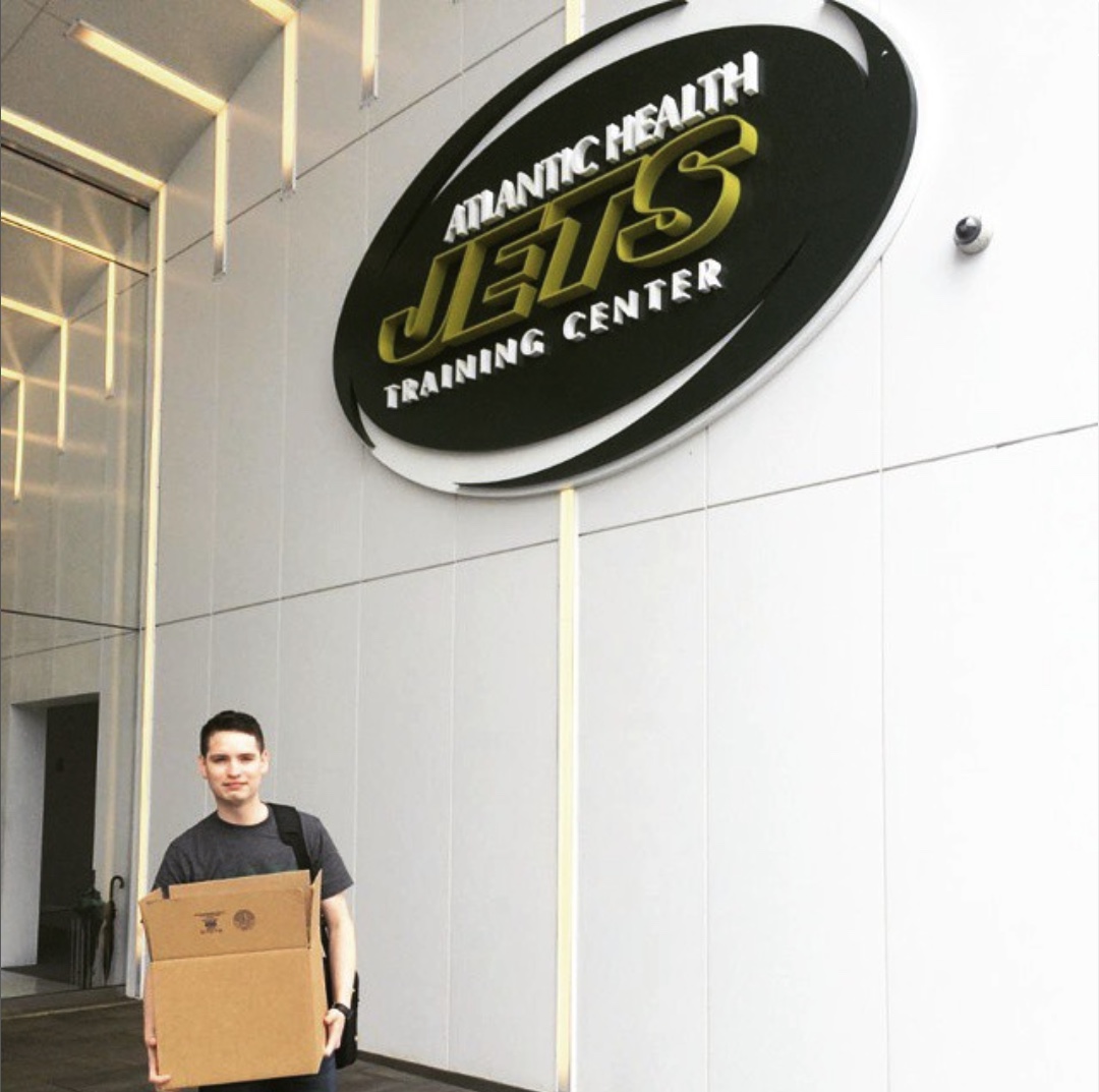 Justin Herrera carrying a box beneath the Atlantic Health Jets Training Center logo on his last day