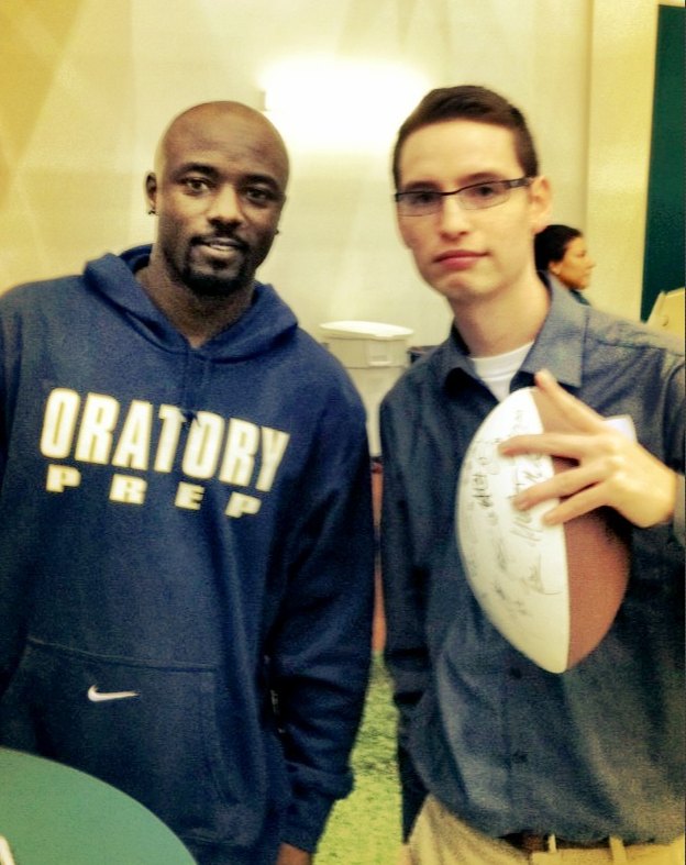 Justin Herrera holding a signed football, standing beside Santonio Holmes at the Jets facility in Florham Park, New Jersey.